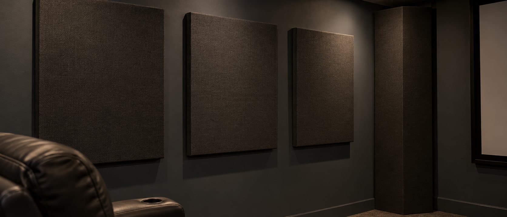 Three charcoal fabric acoustic panels on a dark theater wall with a corner bass trap, a leather recliner in the foreground