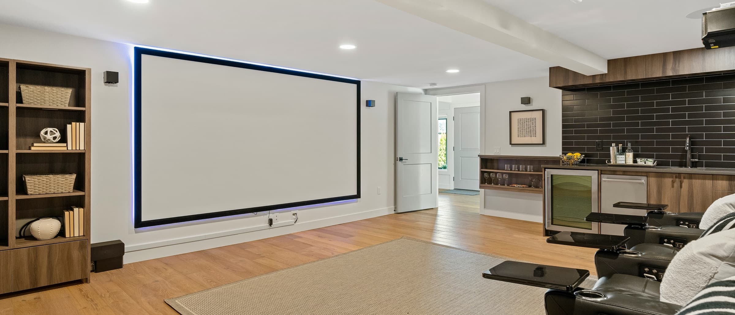 Bright finished basement theater with a fixed-frame screen, recliners, and a bar