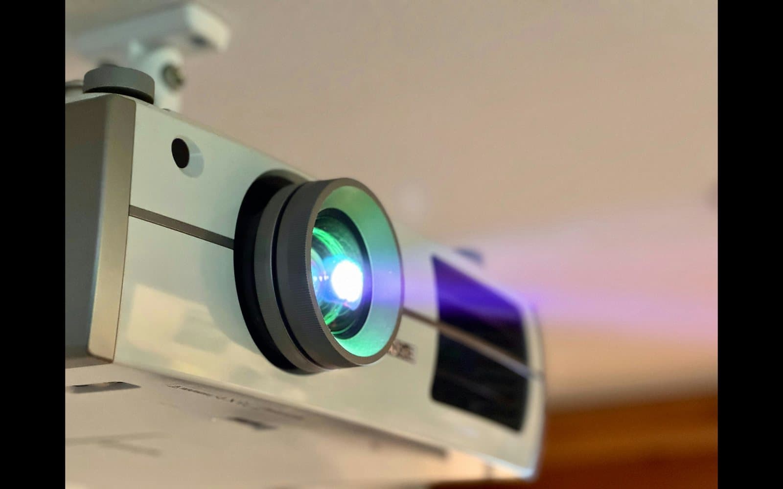 Ceiling-mounted projector with its lens lit, seen from below