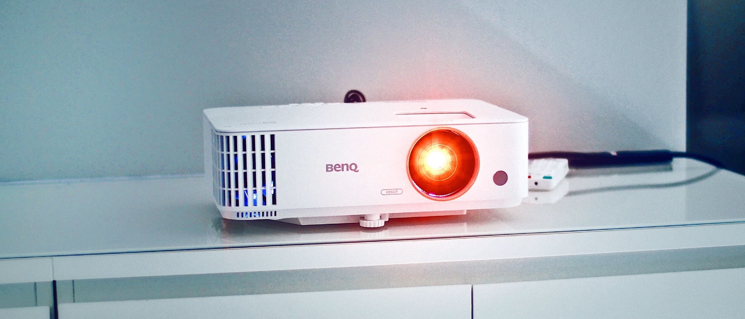 Projector on a white console with its lens glowing