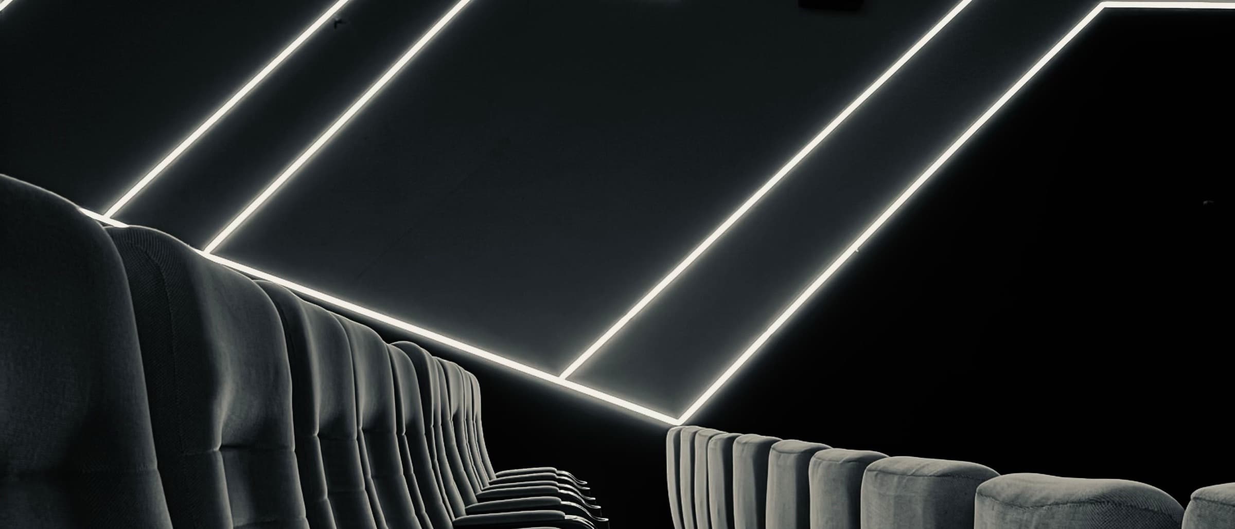 Rows of theater seats beneath wall-mounted surround speakers and angular light lines