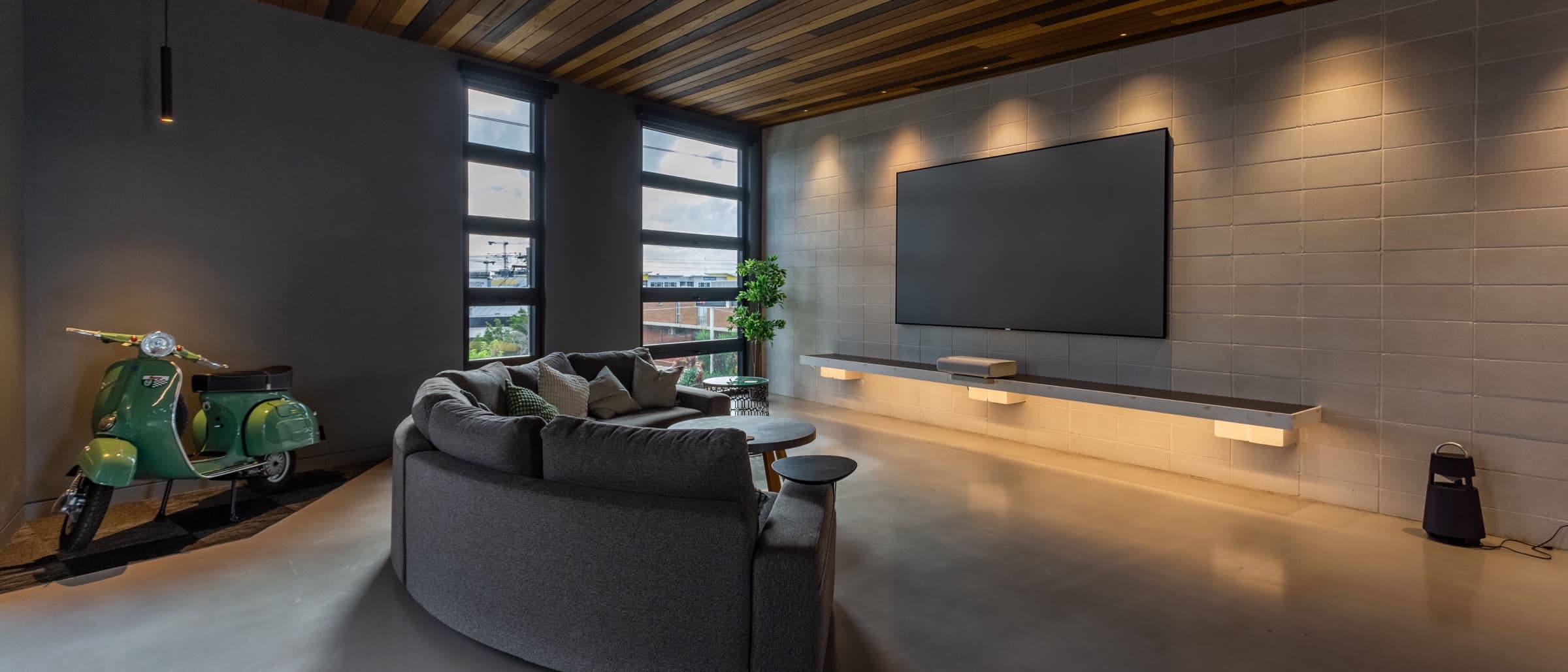 Modern lounge with a large wall-mounted TV, wood ceiling, and curved sofa