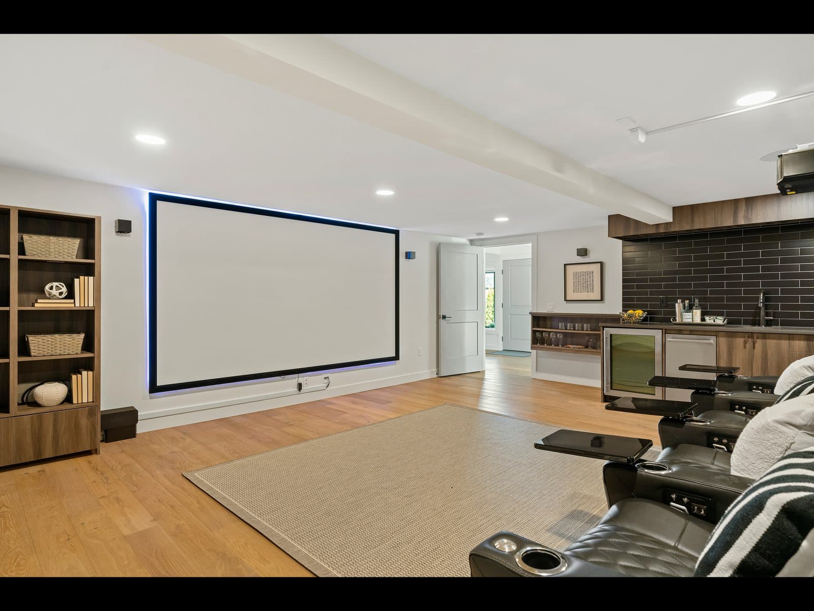 Bright finished basement theater with a fixed-frame screen, recliners, and a bar