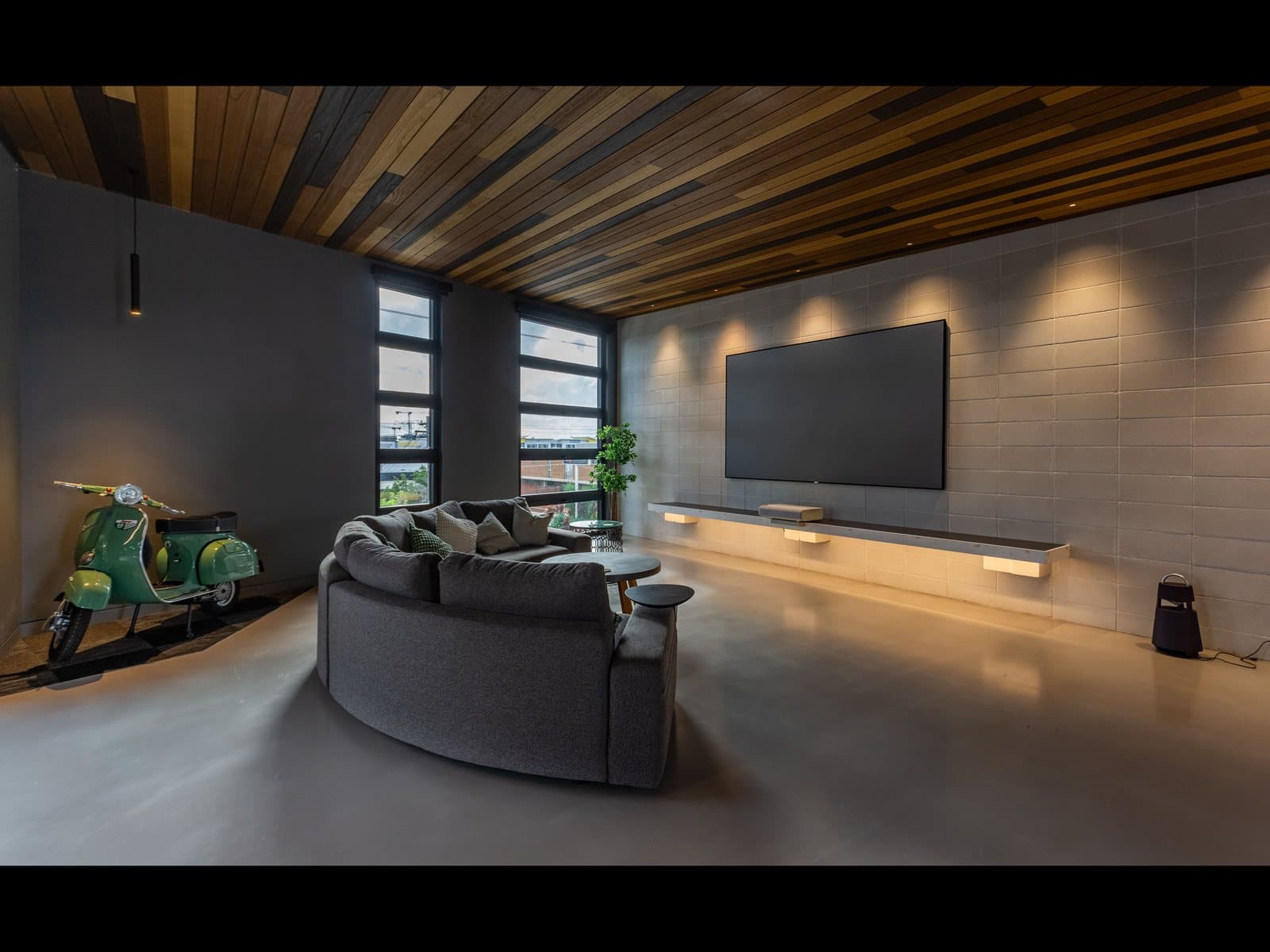Great room with a large wall-mounted TV, wood ceiling, and curved sofa